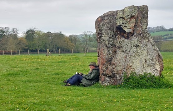 man with a notebook sitting against a large rock