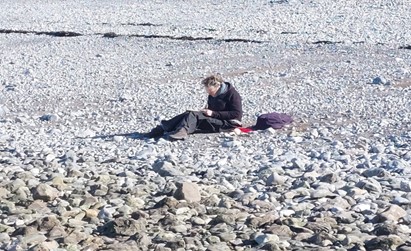 man writing while sitting on a rocky landscape